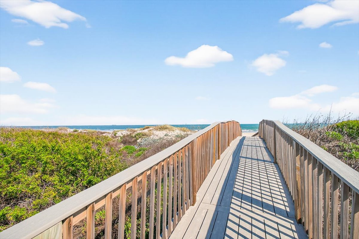Wooden boardwalk leads through coastal dunes to pristine beach access under bright blue skies.