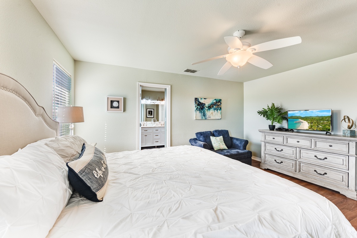 Unwind in your serene master bedroom featuring a plush king bed, cozy reading chair, and tropical artwork that sets the perfect vacation mood.