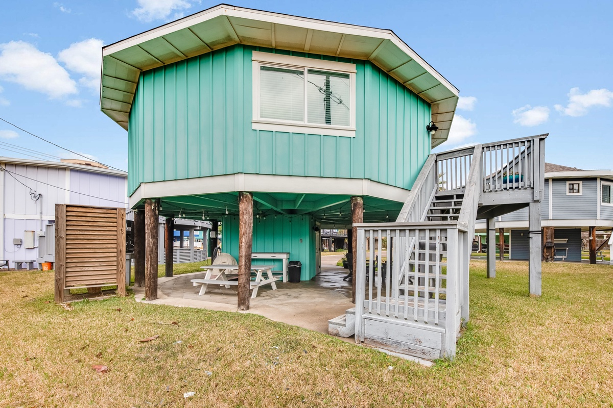 Charming turquoise beach house on stilts with covered patio and outdoor shower, perfect for coastal getaways.