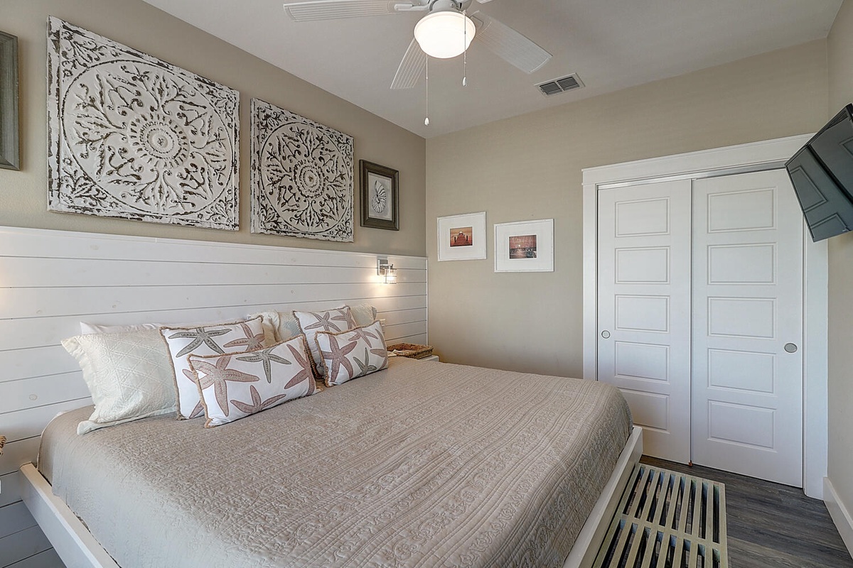 Drift off to sleep in your serene sanctuary with coastal-inspired decor and plush bedding beneath the gentle breeze of a ceiling fan.