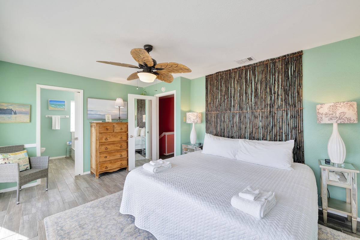 Drift off in your serene coastal bedroom with soothing sea-green walls, crisp white linens, and tropical ceiling fan creating the perfect beach retreat atmosphere.