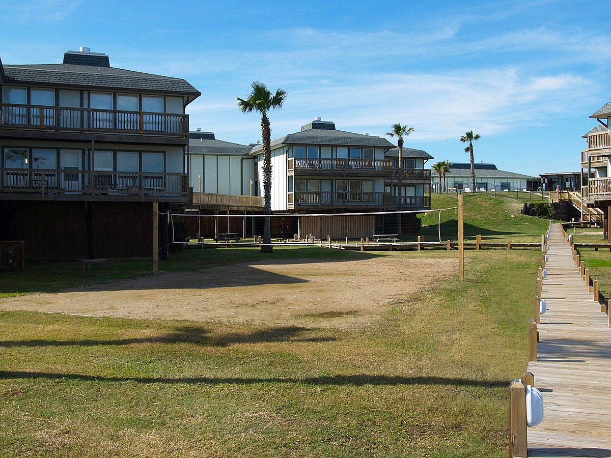 Coastal property complex with multi-level buildings, palm trees, and boardwalk access creating a tropical vacation atmosphere.