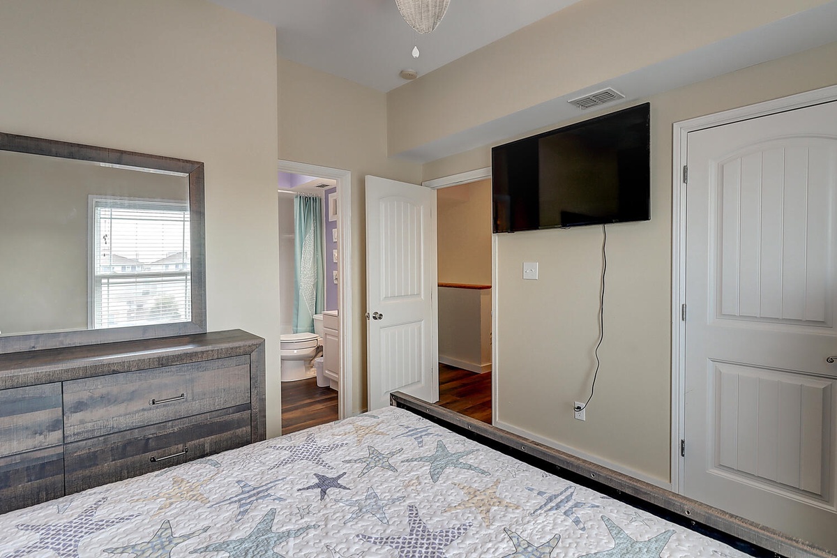 Unwind in your comfortable bedroom featuring a wall-mounted TV, spacious dresser, and convenient wardrobe storage for all your belongings.