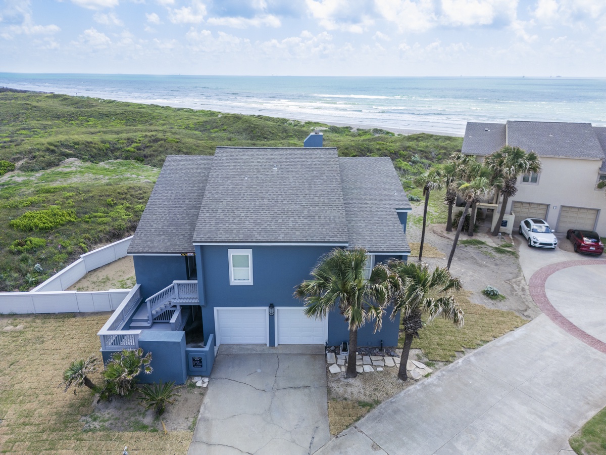 Charming blue beach house nestled between coastal dunes and ocean, offering direct access to pristine shoreline.