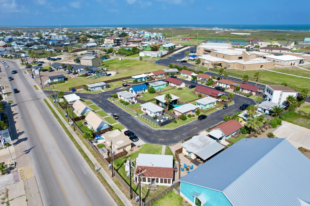 Aerial view of a charming coastal neighborhood with colorful homes, palm trees, and the sparkling ocean just beyond the horizon.