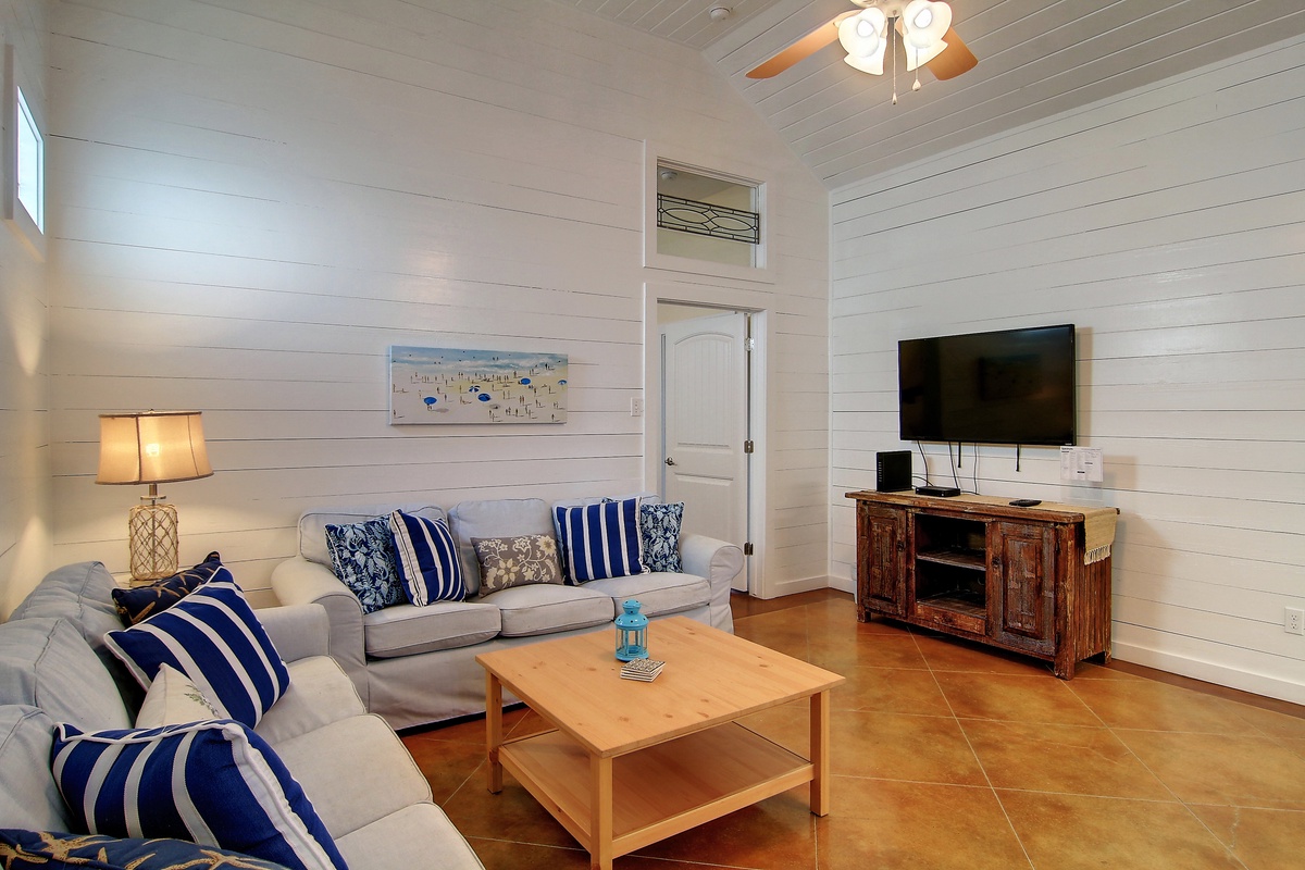 Sink into plush sofas adorned with navy striped pillows in your coastal-inspired living room, complete with entertainment center and warm lighting for perfect relaxation.