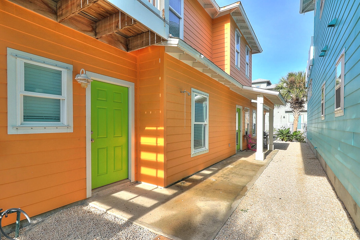 Vibrant coastal home with cheerful orange siding and lime green door, surrounded by colorful beach houses in a charming seaside neighborhood.