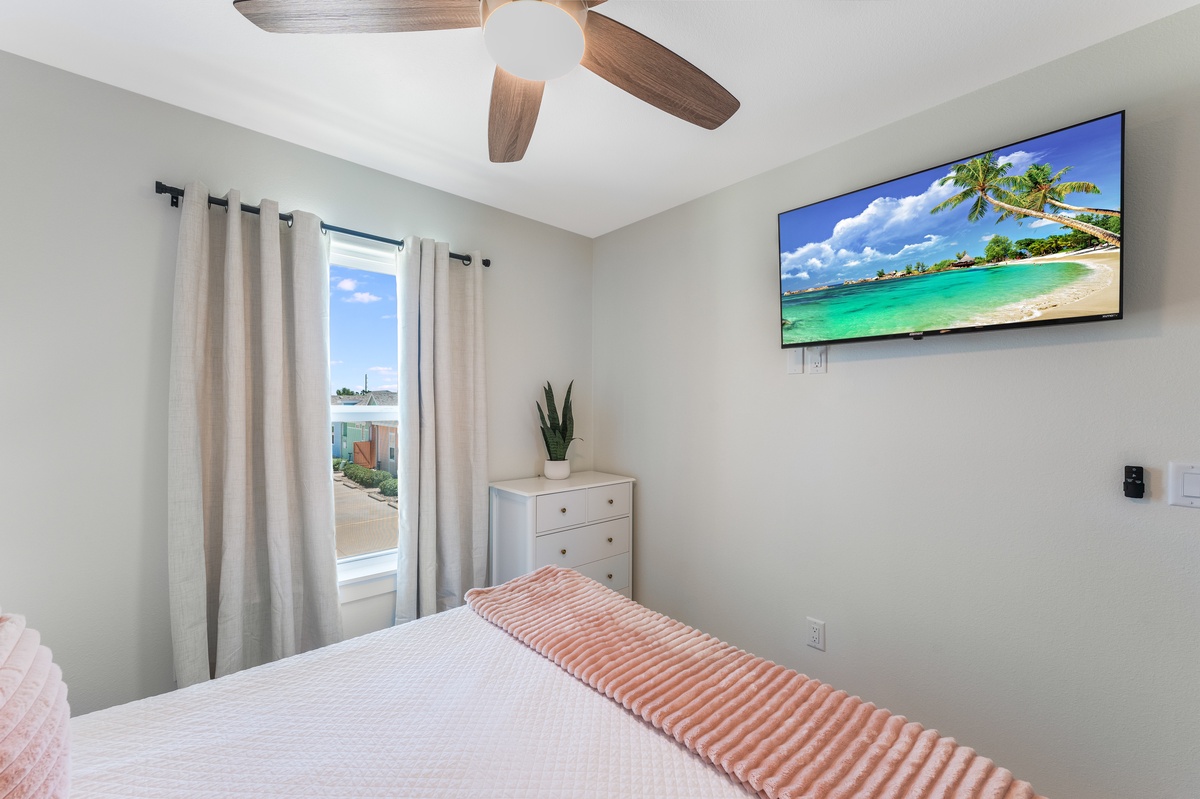 Relax in your peaceful bedroom with a large wall-mounted TV and cooling ceiling fan for ultimate comfort.