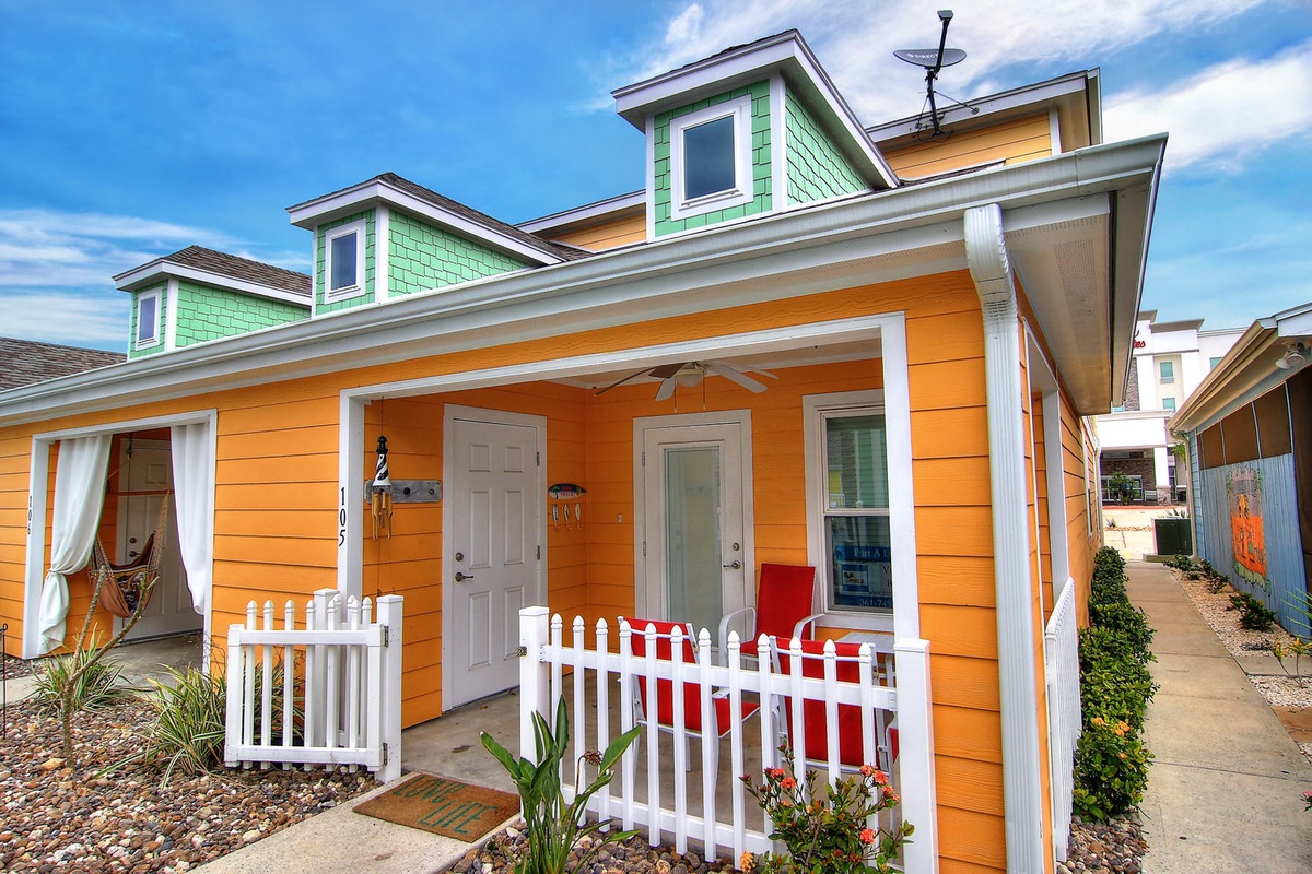 Charming orange cottage with white picket fence and green dormer windows creates a welcoming coastal retreat.