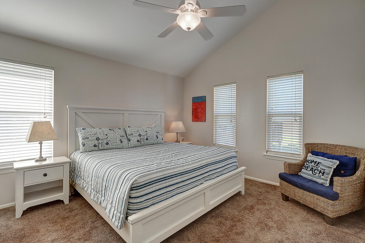 Drift off to sleep in this bright, airy bedroom with coastal-striped bedding and natural light streaming through multiple windows.