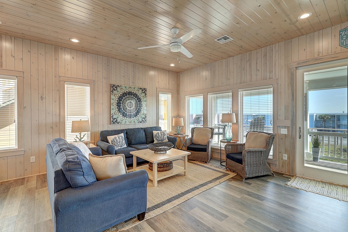 Relax in this coastal living room with warm wood walls, comfortable seating, and ocean views from every window.