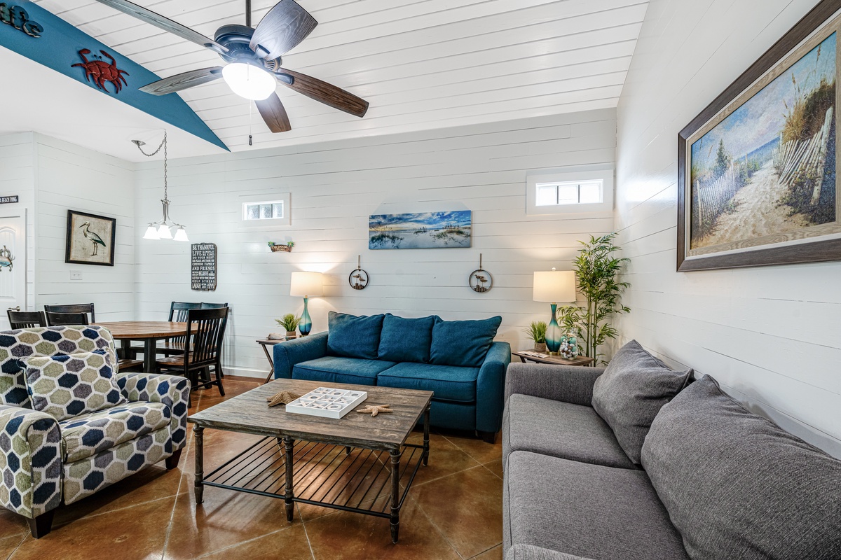 Relax in your bright coastal living room with plush sofas, charming beach decor, and a ceiling fan for comfort.