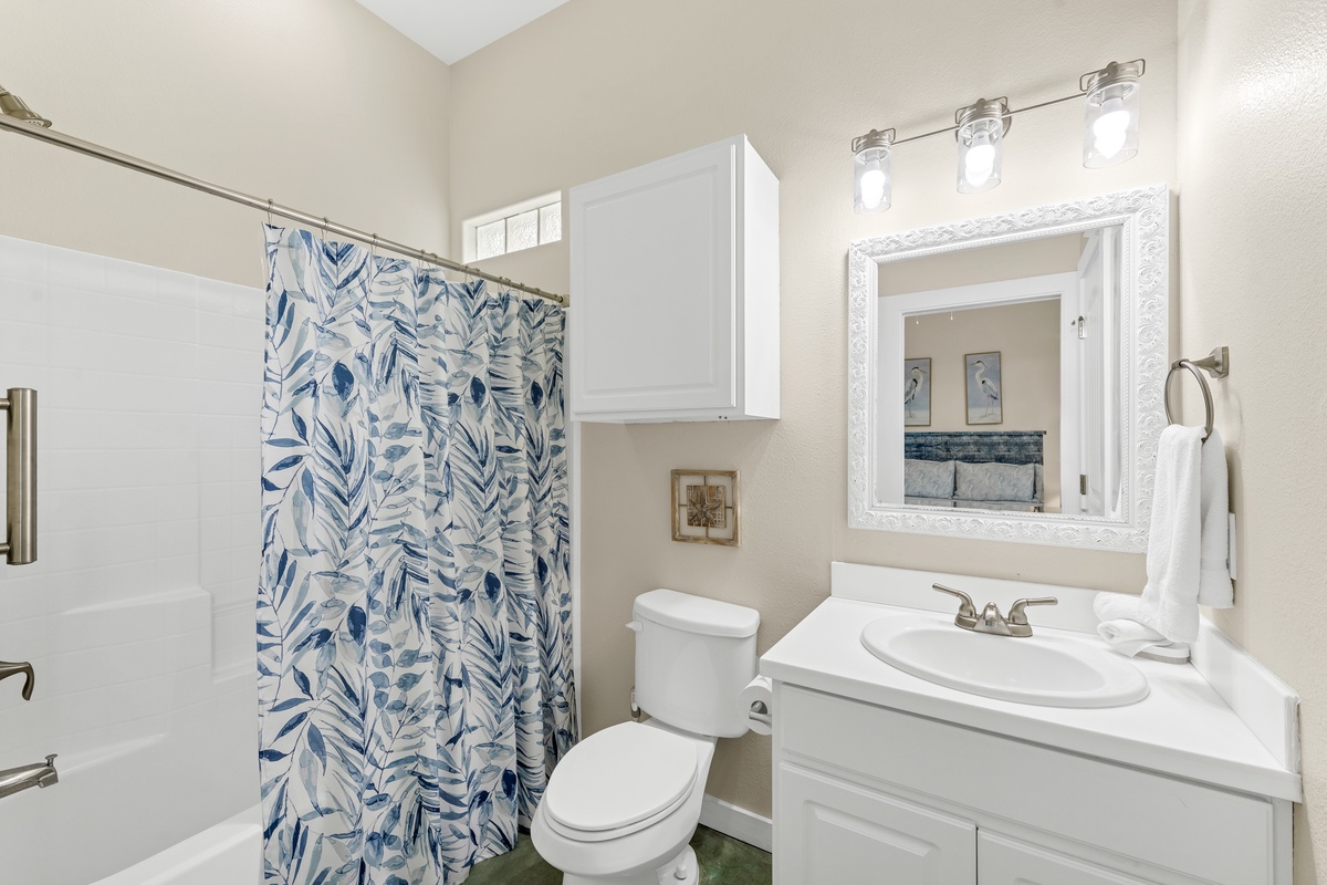 Refresh in your bright, clean bathroom featuring a tub-shower combo, elegant vanity, and cheerful botanical curtain that brings coastal charm to your morning routine.