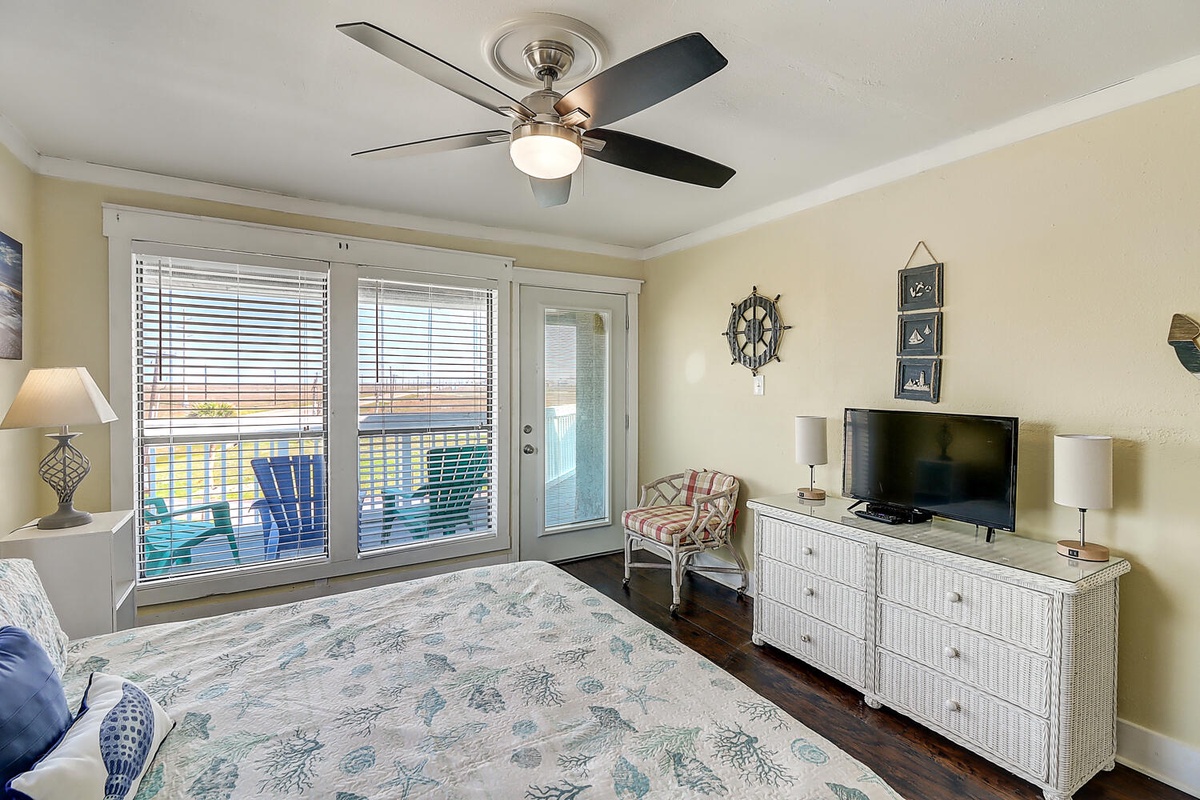 Rest comfortably in your coastal bedroom with ocean-themed decor, ceiling fan, and private balcony access to colorful outdoor seating.