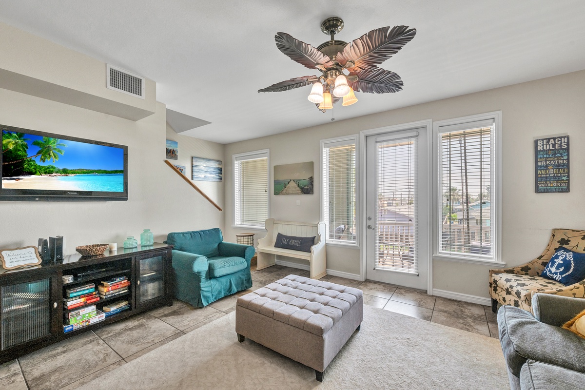 Relax in your bright living space with coastal charm, featuring a tropical ceiling fan and entertainment center for cozy evenings.