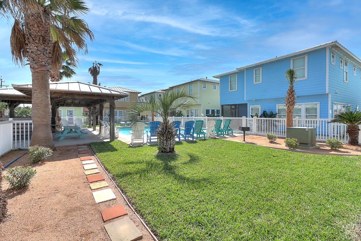 Colorful beach houses surround a pristine pool area with tropical palms and well-maintained lawn space perfect for outdoor gatherings.