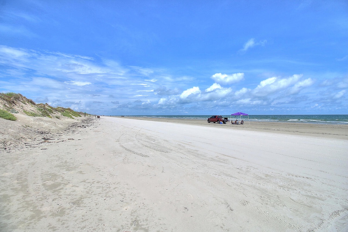 Expansive sandy beach stretches along the coastline with dunes and ocean views under bright blue skies.