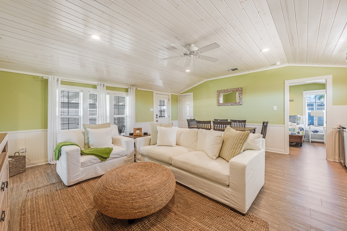 Unwind in your spacious living room with plush white sofas, charming green walls, and a gorgeous wood plank ceiling that creates the perfect coastal retreat atmosphere.