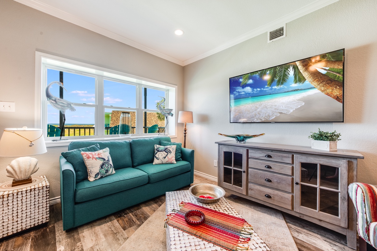 Relax on your plush teal sofa while watching the large TV, surrounded by coastal-inspired decor and natural light streaming through your windows.