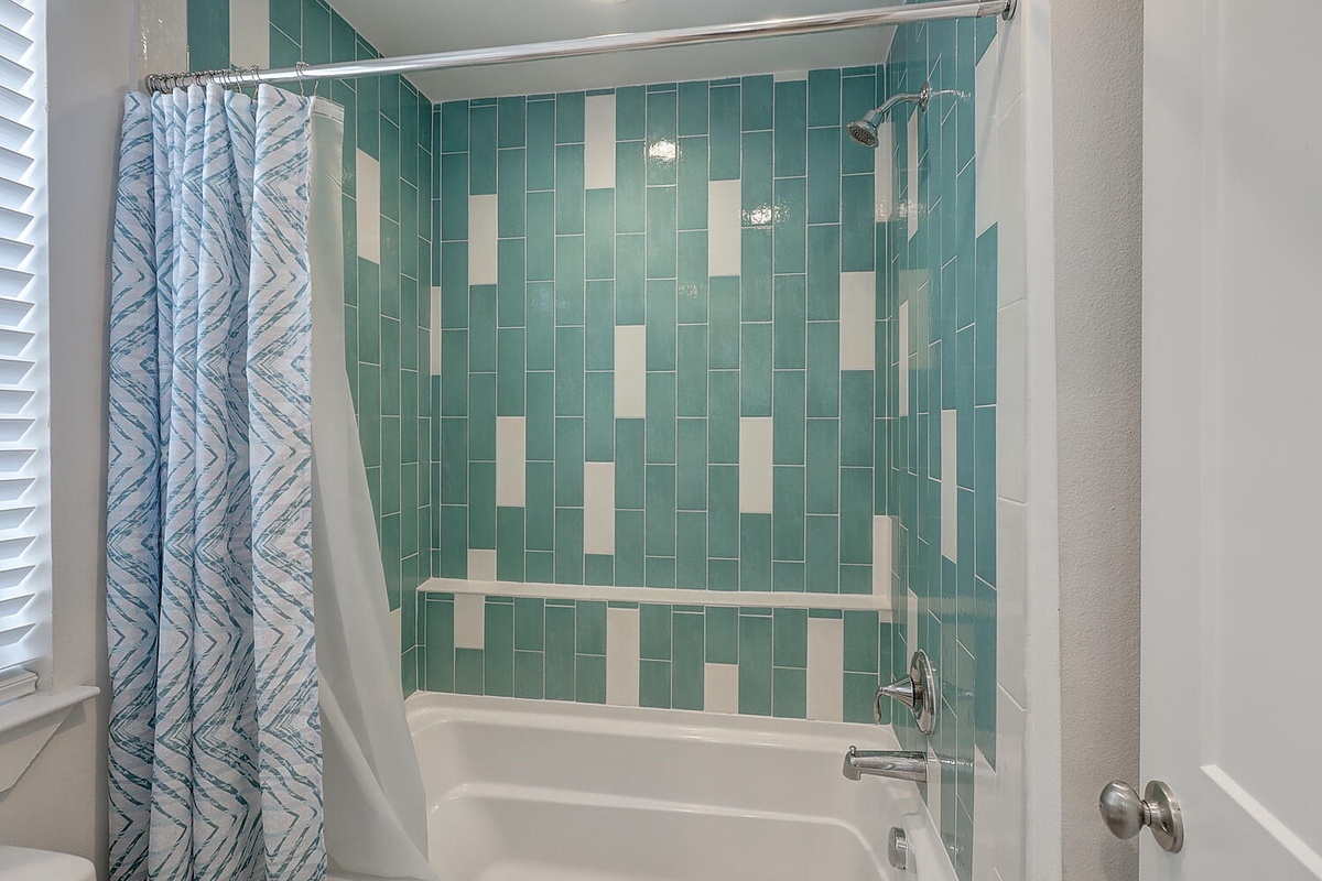 Step into your stylish bathroom featuring vibrant turquoise tile work and a relaxing tub-shower combo for unwinding after exploring.