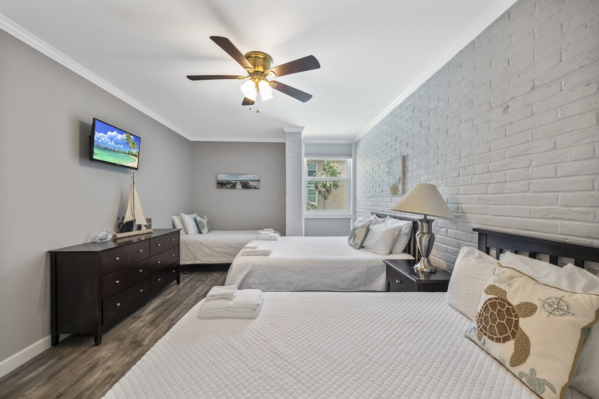 Rest comfortably in your stylish bedroom with twin beds, exposed brick walls, and modern amenities including ceiling fan and TV.