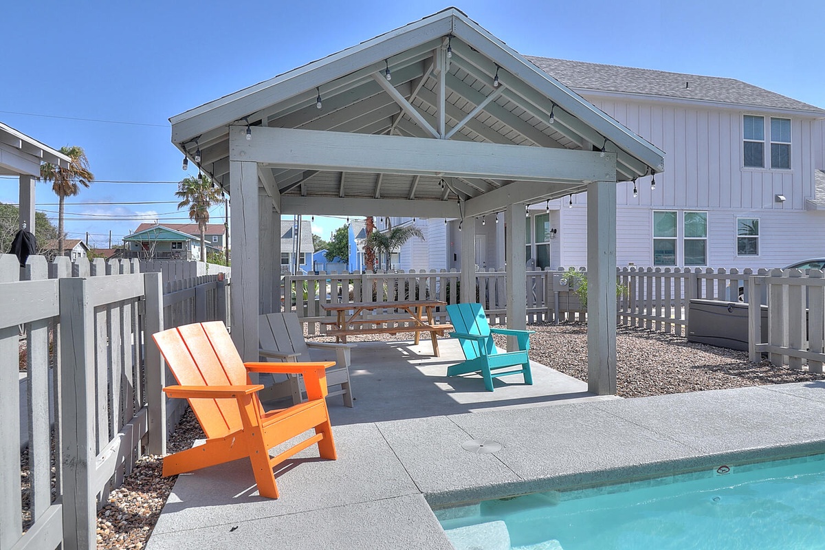 Bright outdoor pavilion with colorful seating overlooks the sparkling pool area in this coastal vacation home setting.