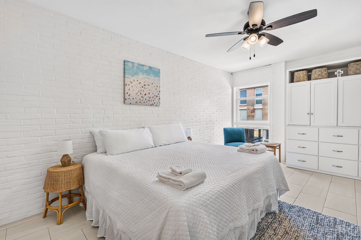 Sink into crisp, comfortable linens in your serene bedroom, where a gentle ceiling fan and calming coastal art create the perfect beach retreat vibe.