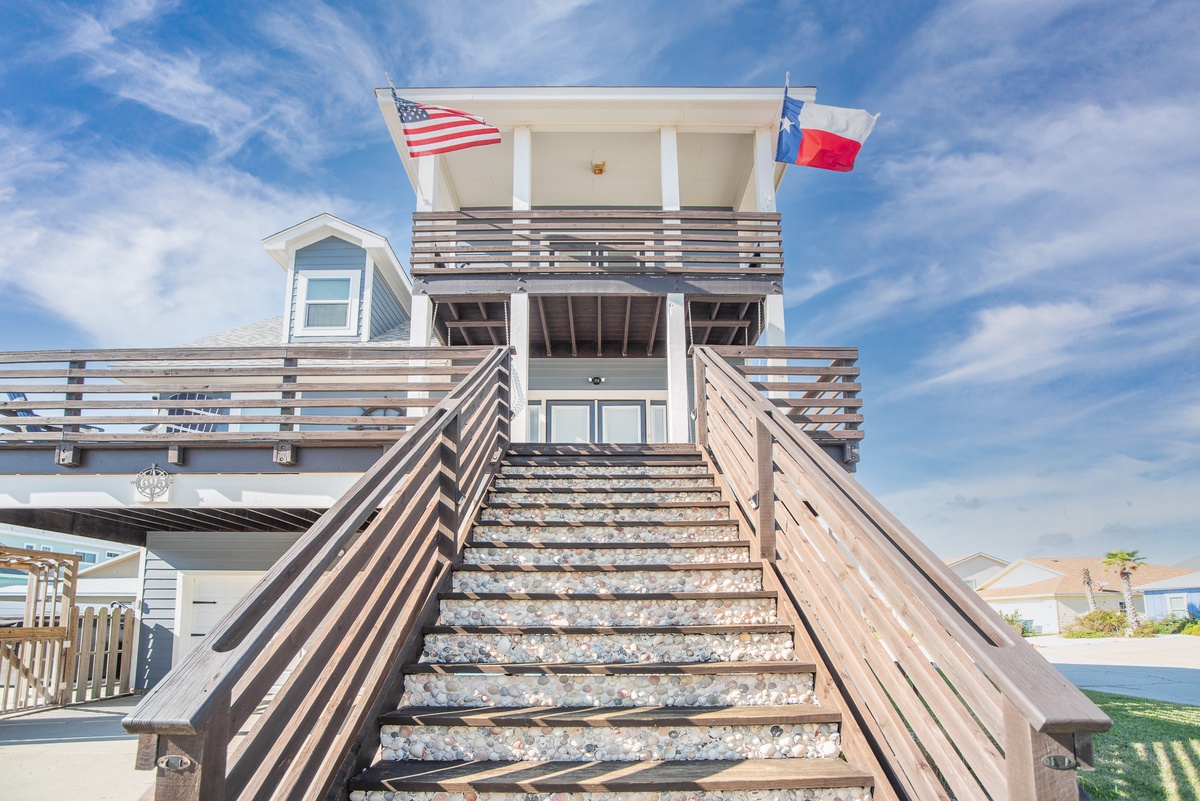 Modern coastal property featuring distinctive architecture with American and Texas flags flying proudly above the entrance deck.