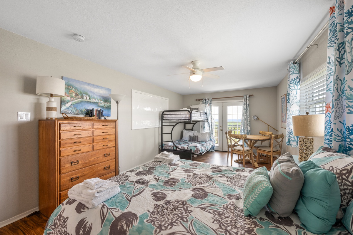 Your cozy retreat awaits with comfortable sleeping arrangements, warm wood furnishings, and a cheerful coastal palette. The small dining table is perfect for morning coffee while natural light streams in through the glass doors.