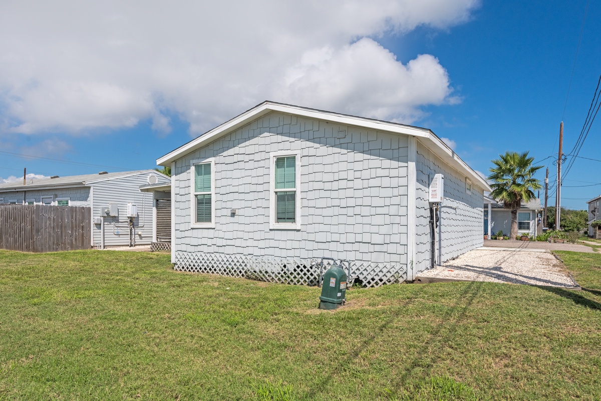 Charming white cottage with tropical palms nearby, featuring a spacious lawn and convenient parking area for your coastal getaway.