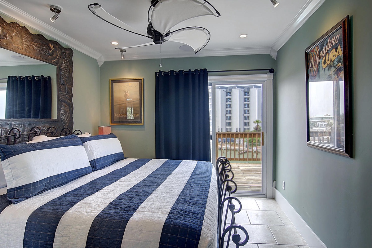 Drift off in this coastal-themed bedroom with its unique ceiling fan, blue striped bedding, and private balcony access.