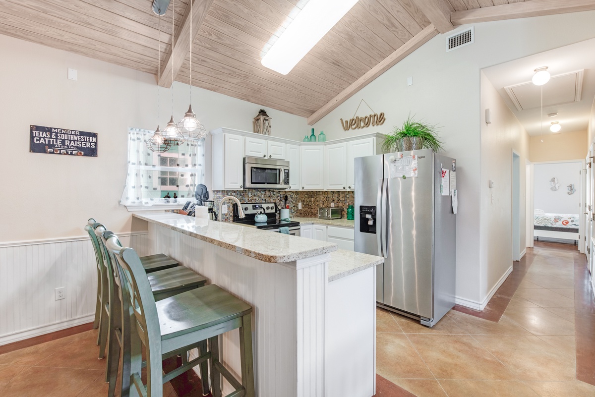 Your fully equipped kitchen awaits with granite counters, stainless appliances, and coastal charm under soaring wood-beam ceilings.