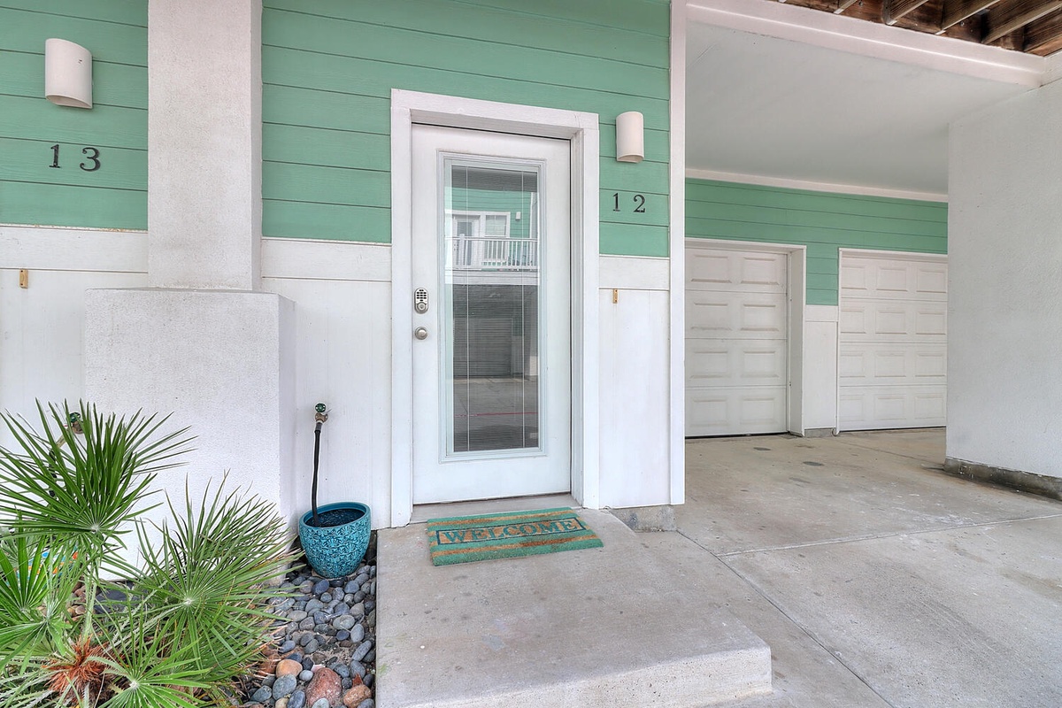 Modern coastal entrance with tropical plants welcomes guests to unit 12. Clean lines and cheerful mint green siding create an inviting arrival.