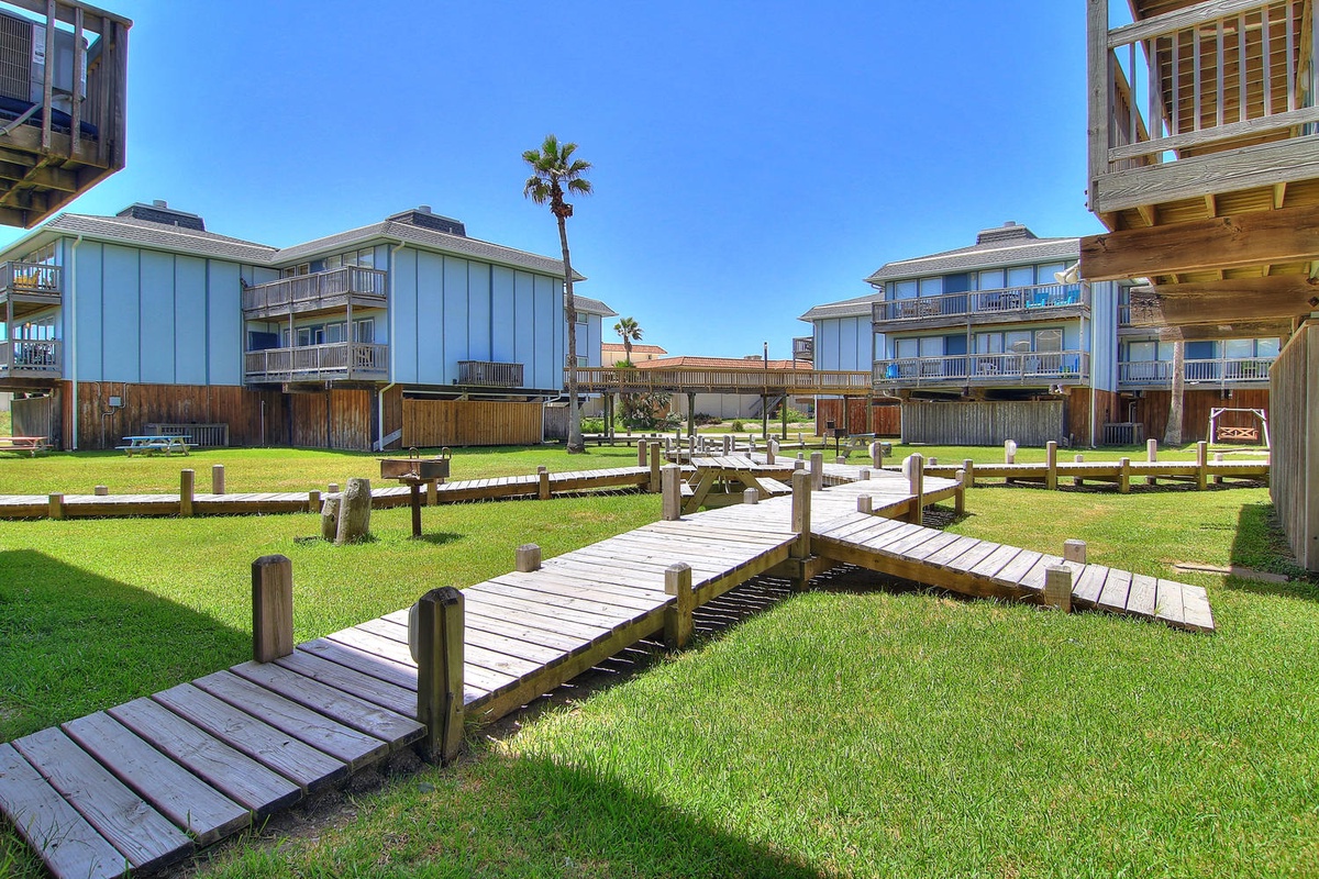 Charming beachfront property complex with scenic wooden walkways winding through manicured lawns and tropical palm trees.