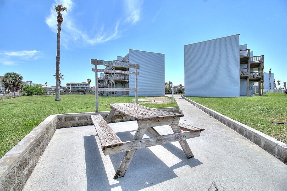 Picnic table on concrete patio with modern beachfront buildings and palm trees in peaceful coastal setting.