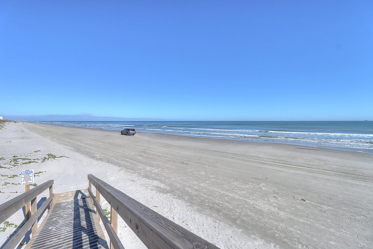 Expansive sandy beach stretches along the coastline with gentle waves rolling ashore under clear blue skies.
