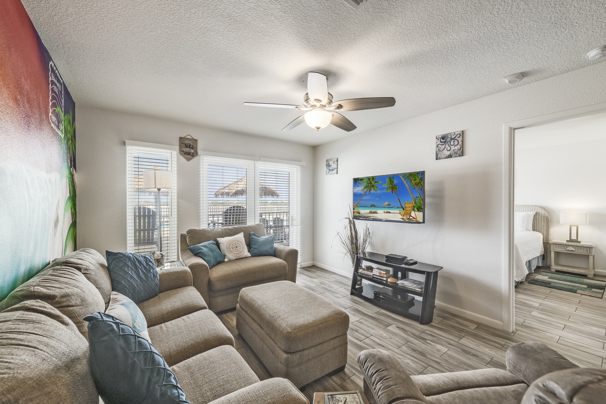 Relax in your spacious living room with plush seating, a flat-screen TV, and cheerful beach artwork. Cool ceiling fans and natural light create a welcoming retreat after your adventures.