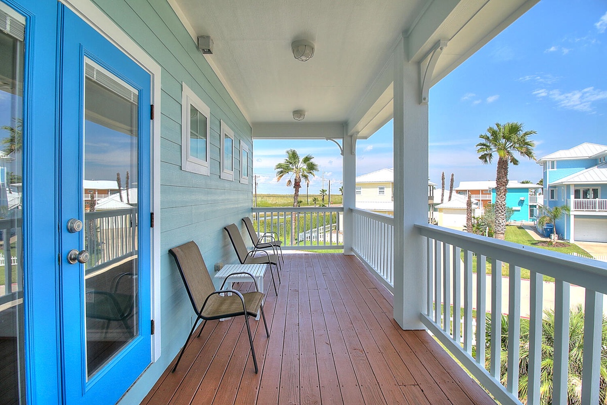 Relax on your private covered porch with cozy seating, overlooking tropical palms and colorful beach houses in this coastal paradise.