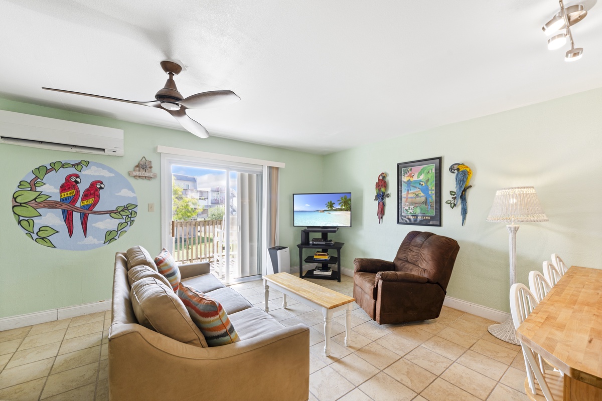 Relax in your bright, tropical-themed living space with colorful parrot artwork, comfortable seating, and peaceful balcony views.