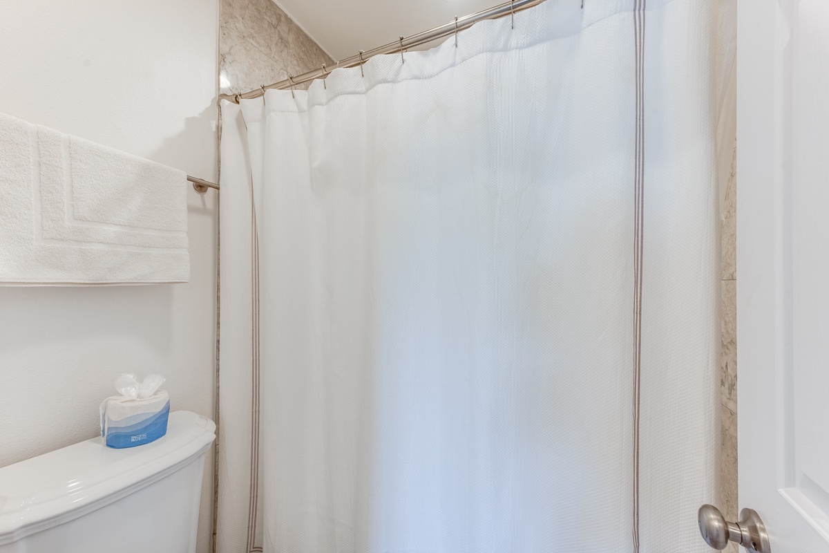 Refresh yourself in this clean, well-appointed bathroom featuring a spacious shower with crisp white curtain and thoughtful amenities.