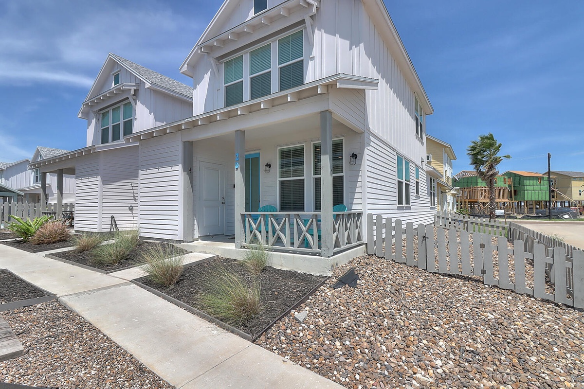 Charming coastal cottage with crisp white siding and turquoise accents, featuring a welcoming front porch in a beachside neighborhood.