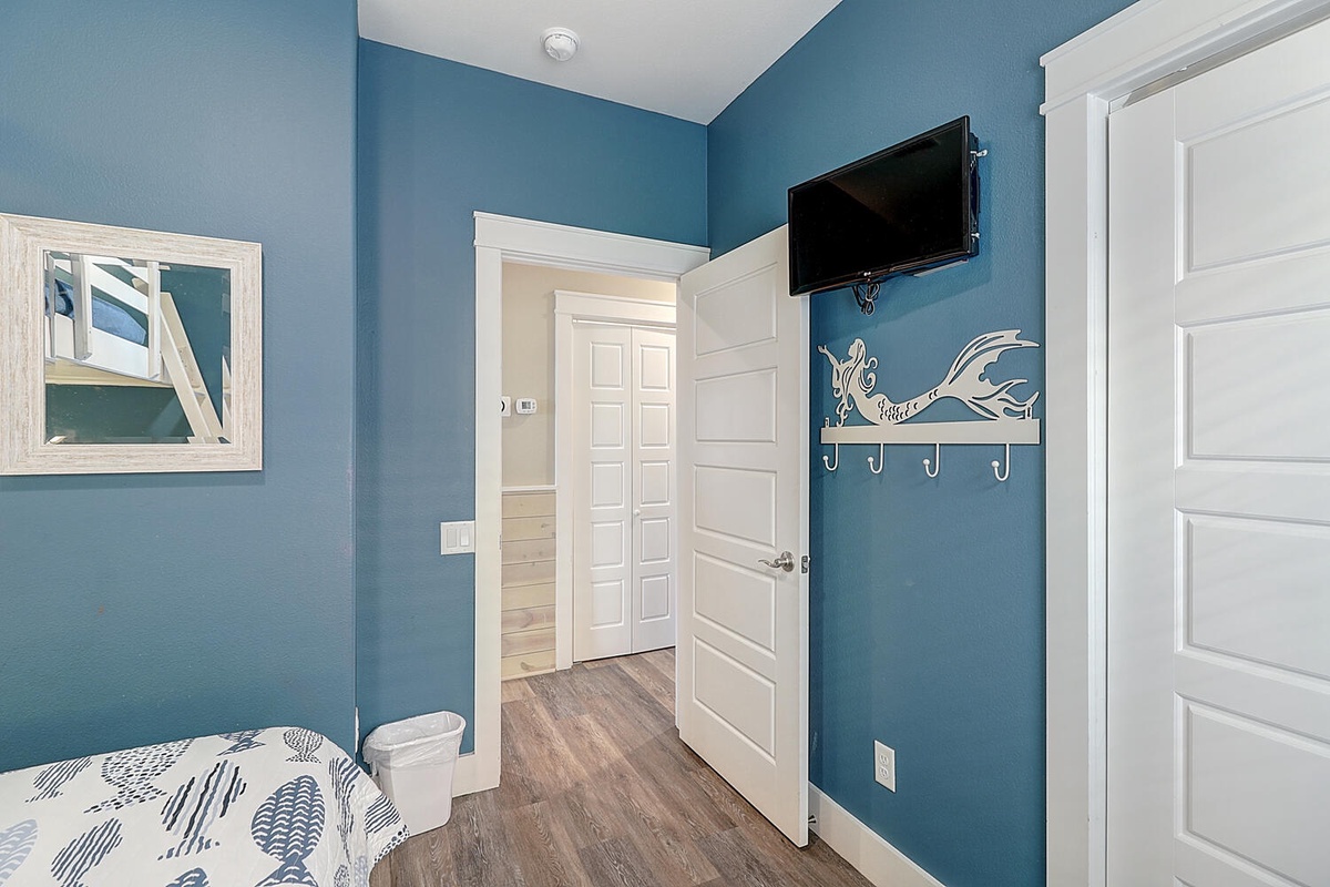 Your coastal-themed bedroom awaits with ocean blue walls, mounted TV, and charming whale hooks for your belongings.