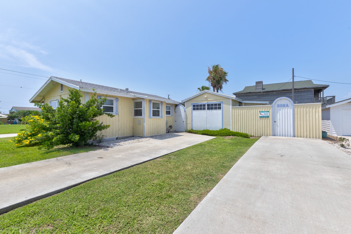 Charming single-story coastal property with a large driveway, lush lawn, and private storage shed in a quiet residential neighborhood.