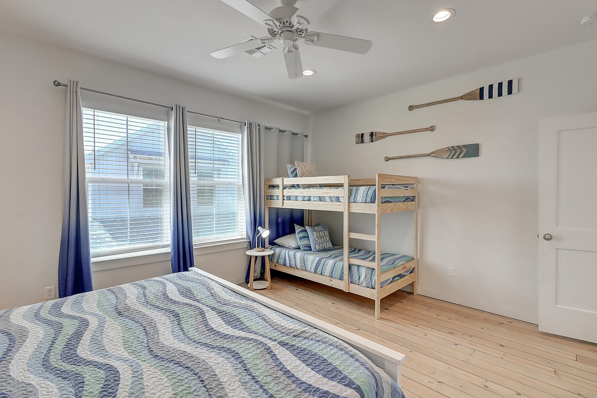 Rest well in your nautical-themed bedroom featuring a queen bed and fun bunk beds, perfect for families with gentle breezes from the ceiling fan.