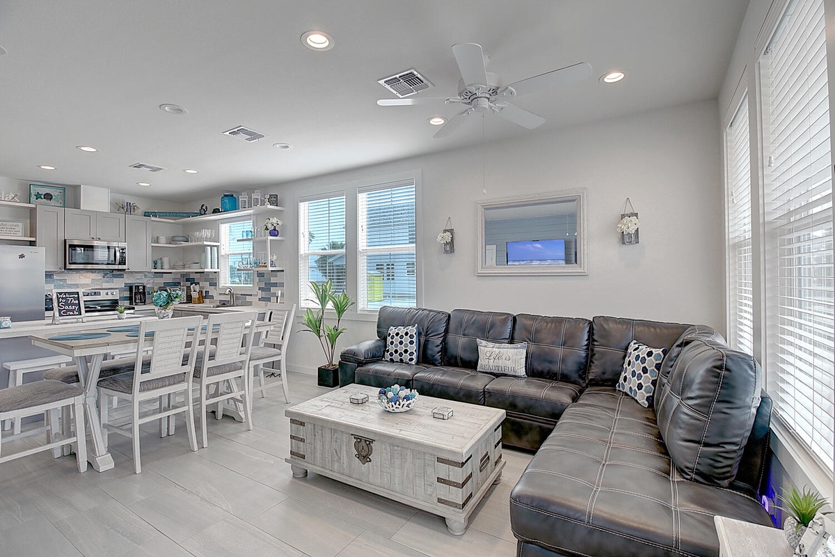 Relax in your open-concept living space featuring a plush leather sectional, fully equipped kitchen, and coastal decor that creates a perfect beach getaway.
