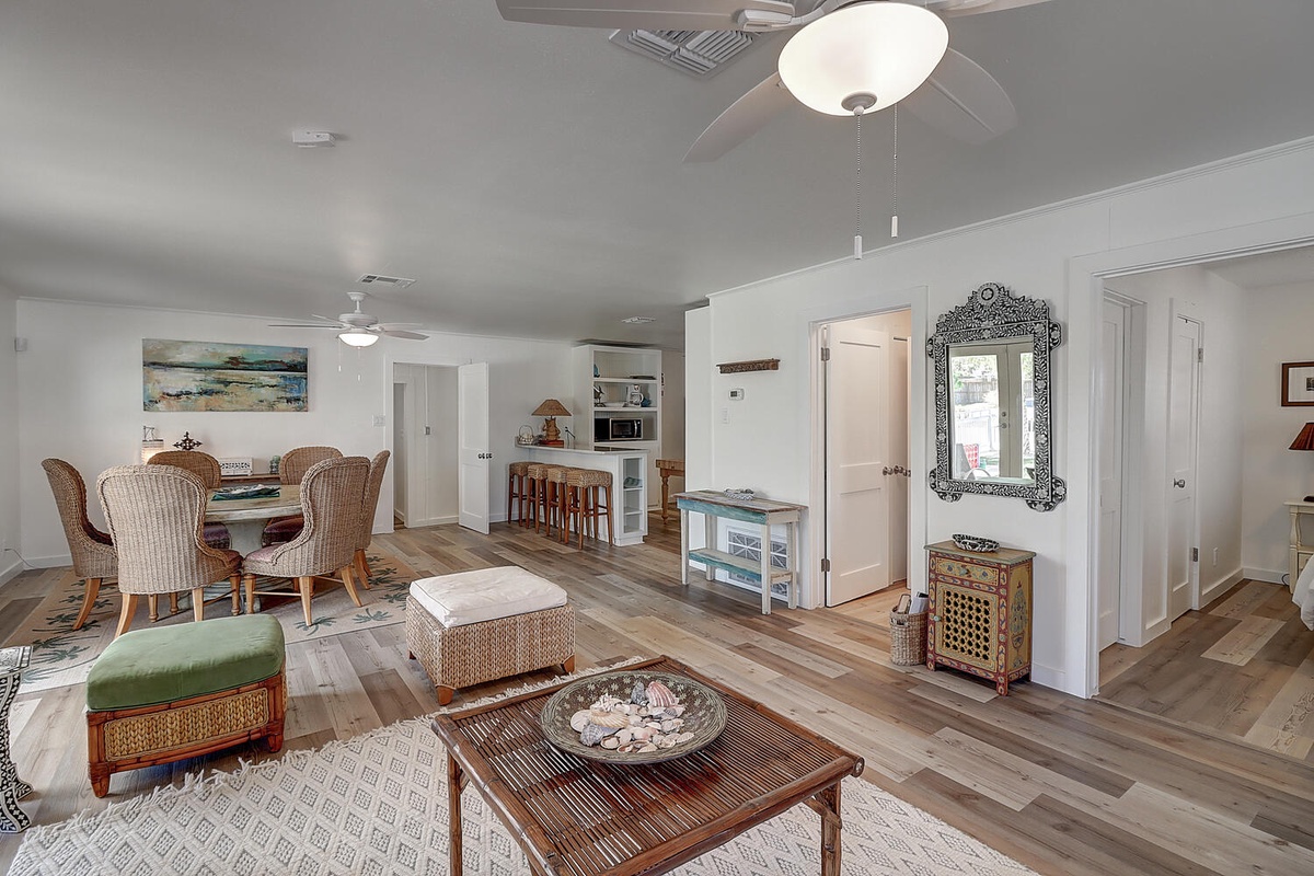 Relax in your spacious open-concept living area with coastal charm, featuring comfortable wicker seating and a breezy ceiling fan for perfect comfort.