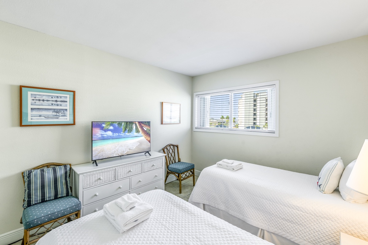Sink into crisp white linens in your peaceful twin bedroom, where morning light filters through blinds and coastal art sets a serene tone.
