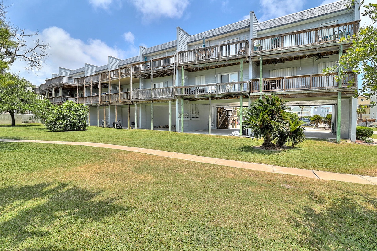 Multi-level waterfront building with spacious balconies surrounded by manicured lawns and tropical landscaping.