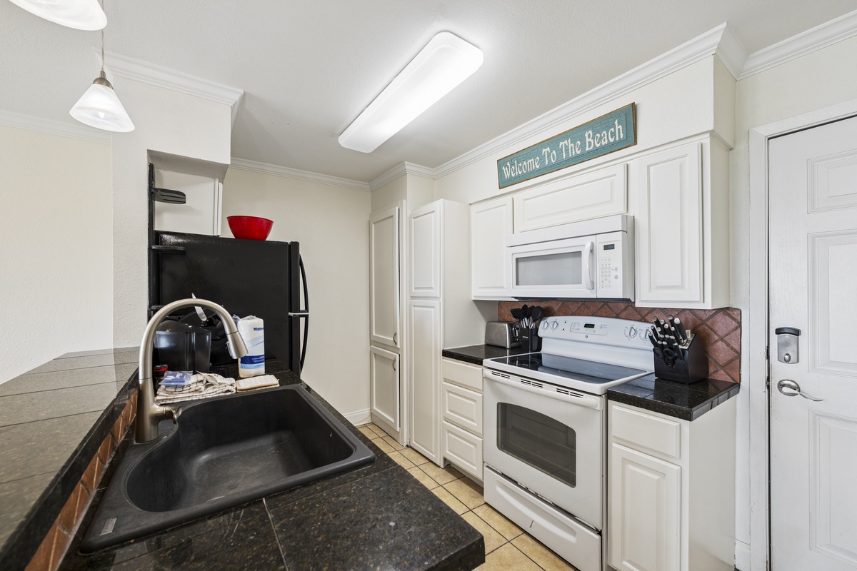 Step into your fully equipped kitchen, complete with modern appliances and beach vibes. Dark granite counters, white cabinetry, and everything you need to whip up your favorite meals. Notice that welcoming beach sign overhead!