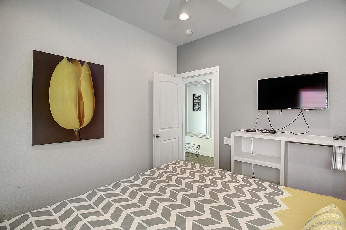 Rest peacefully in your stylish bedroom featuring modern decor, a large TV for entertainment, and cheerful yellow accents creating a warm, welcoming atmosphere.